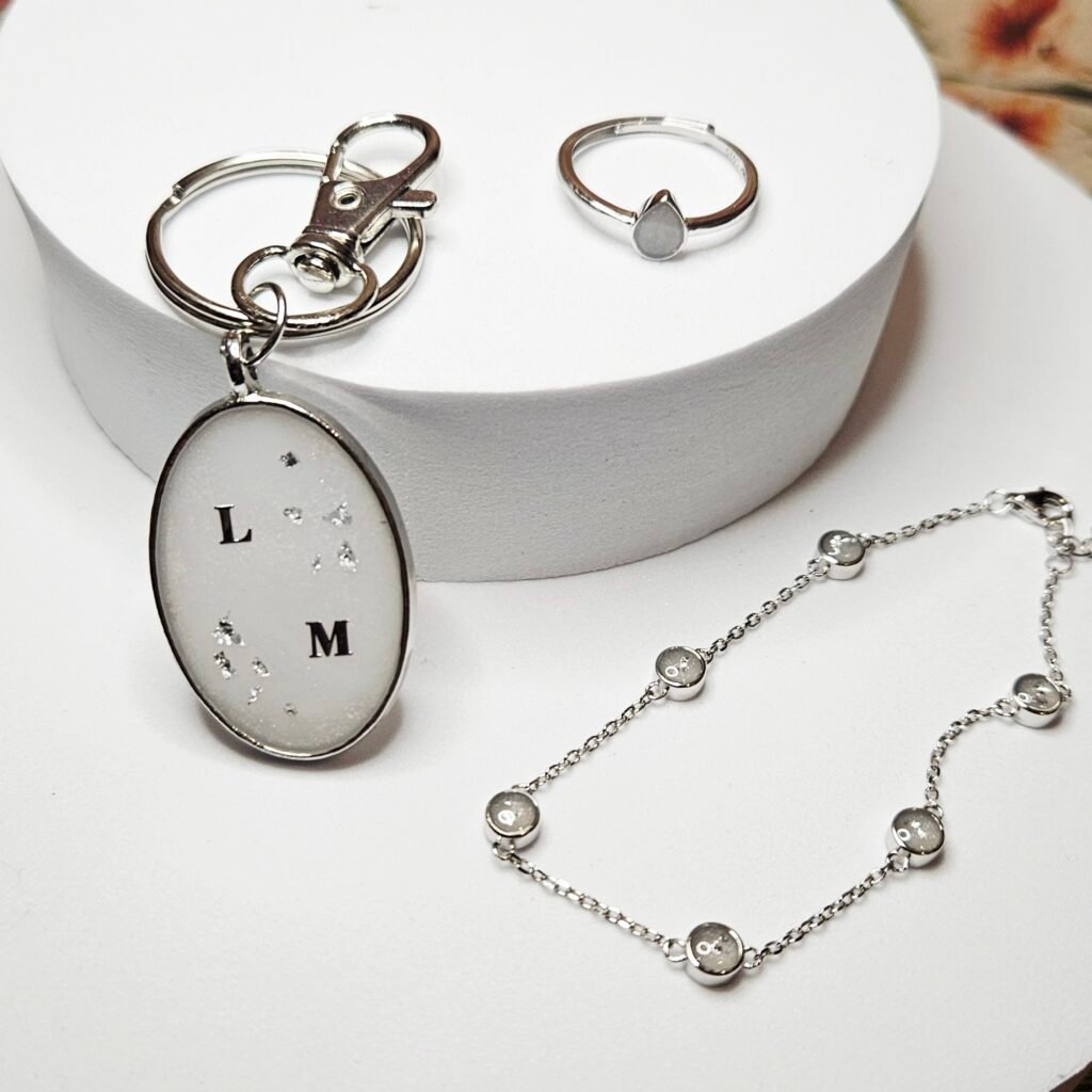 Muttermilchschmuck in Silber: ovaler Schlüsselanhänger mit den Initialen „L" und „M", dazu Ring und Armband, aus dem Workshop in Wuppertal