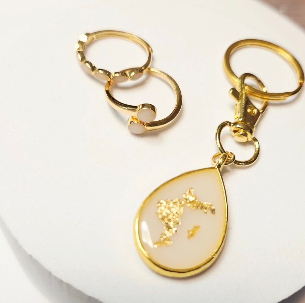 Muttermilchschmuck in Gold: tropfenförmiger Schlüsselanhänger mit Blattgold und zwei Ringe, aus dem Workshop in Wuppertal