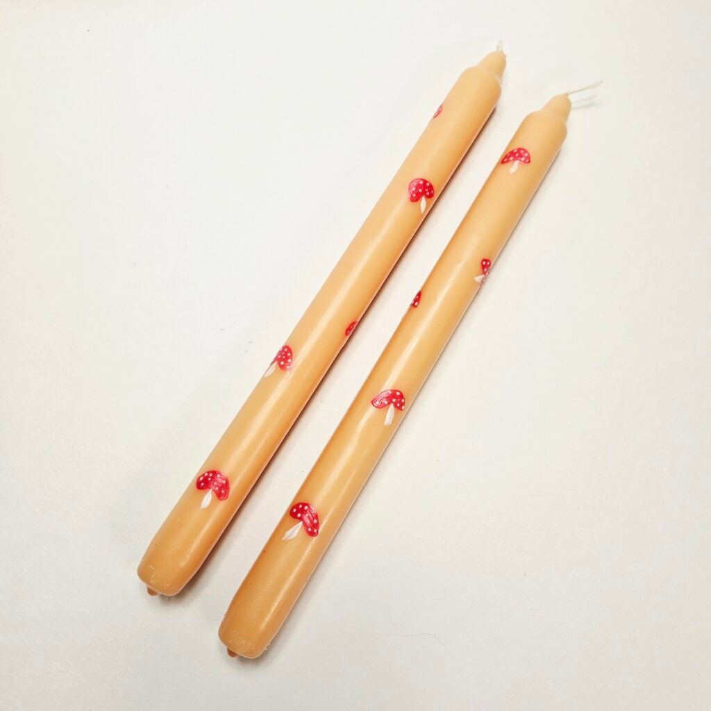 Zwei beige Stabkerzen mit handgemalten roten Fliegenpilzen mit weißen Punkten