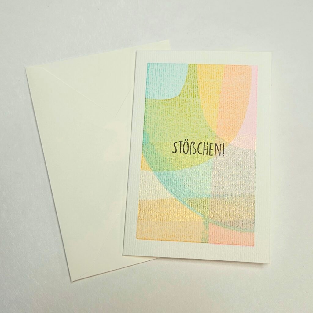 Handbemalte Grußkarte mit pastelligen Farbflächen in Türkis, Gelb und Apricot und dem Schriftzug „Stößchen!", aus dem DIY-Style-Cards-Workshop in Wuppertal