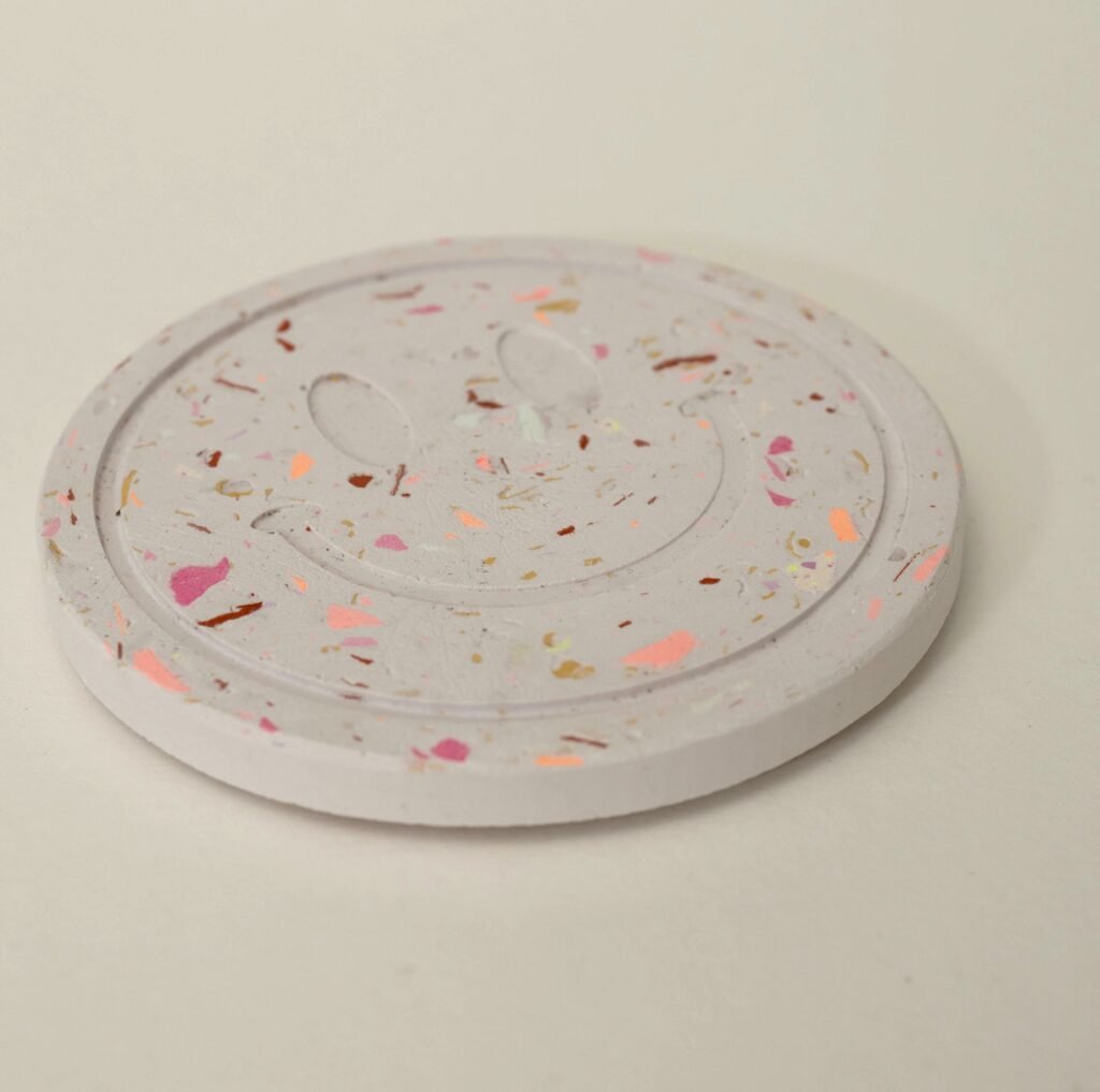Runder Untersetzer aus Gießkeramik im Terrazzo-Look mit Smiley-Relief und bunten Farbsprenkeln, aus dem Workshop in Wuppertal