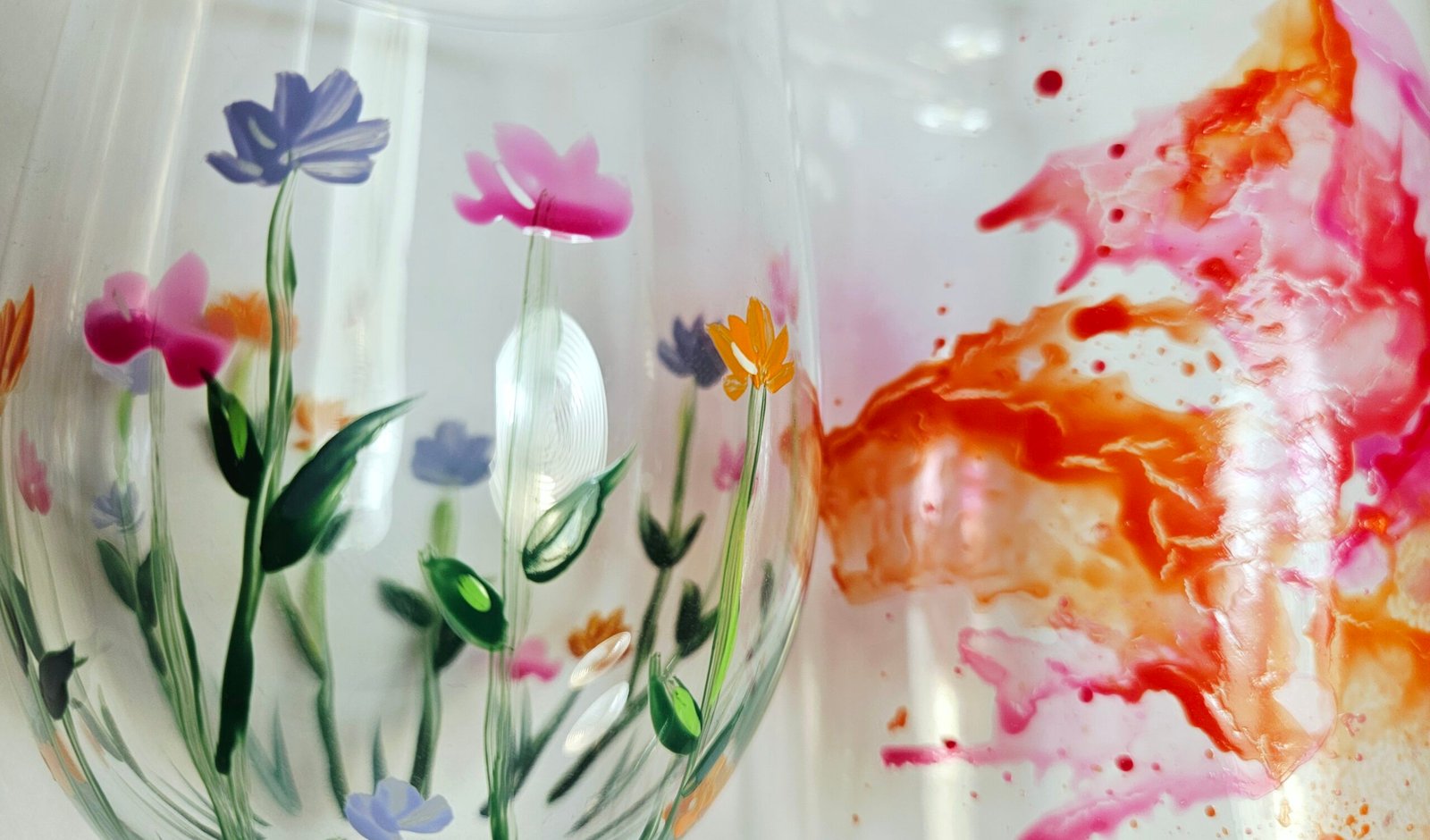 Nahaufnahme bemalter Gläser mit handgemalten Wiesenblumen und abstraktem Farbverlauf in Orange und Pink, aus dem Workshop Gläser bemalen in Wuppertal