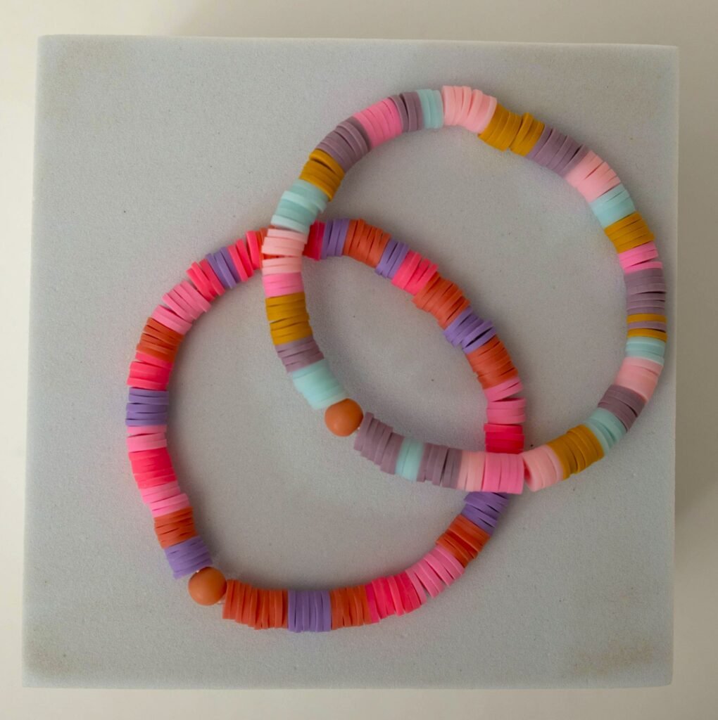 Zwei Armbänder aus Heishi-Perlen in Rosa, Flieder, Koralle, Senfgelb und Mint mit terrakottafarbener Kugel