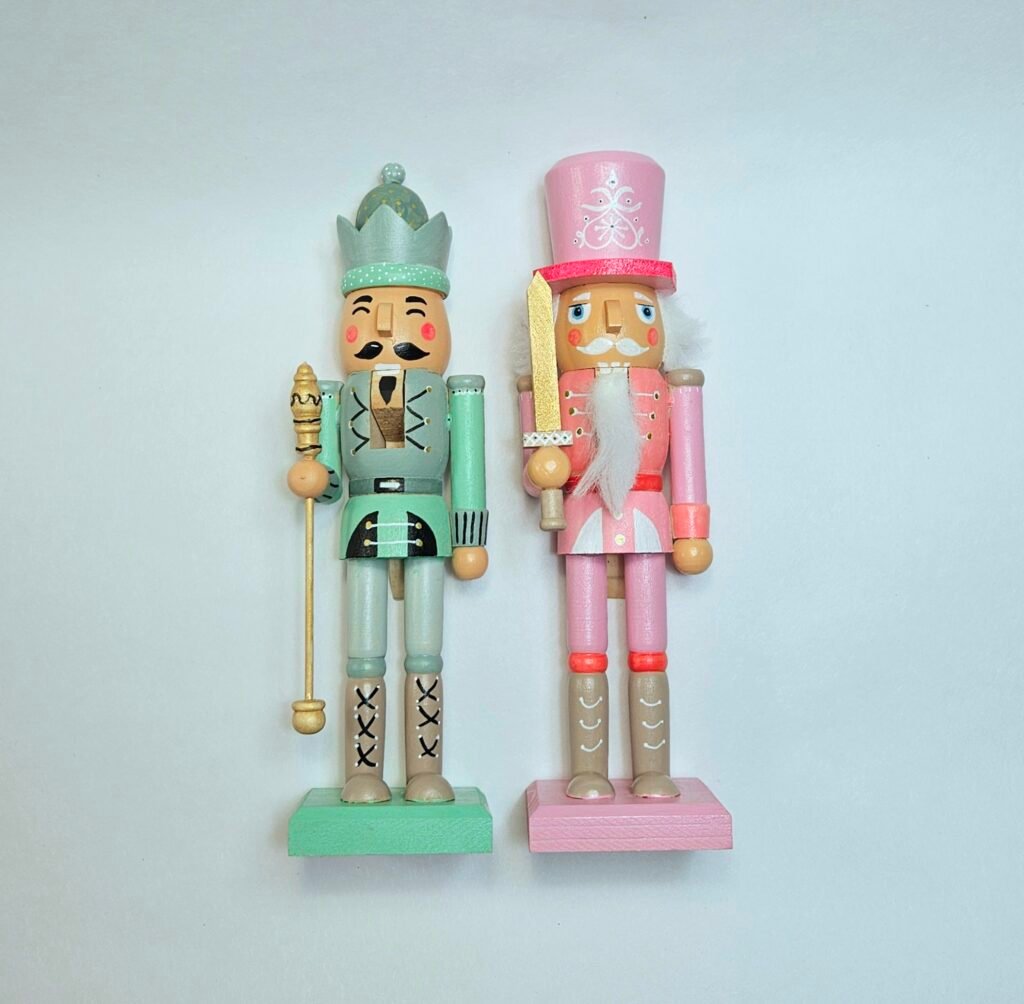 Zwei selbst bemalte Nussknacker nebeneinander, einer in Mintgrün mit Zepter, einer in Rosa mit goldenem Schwert