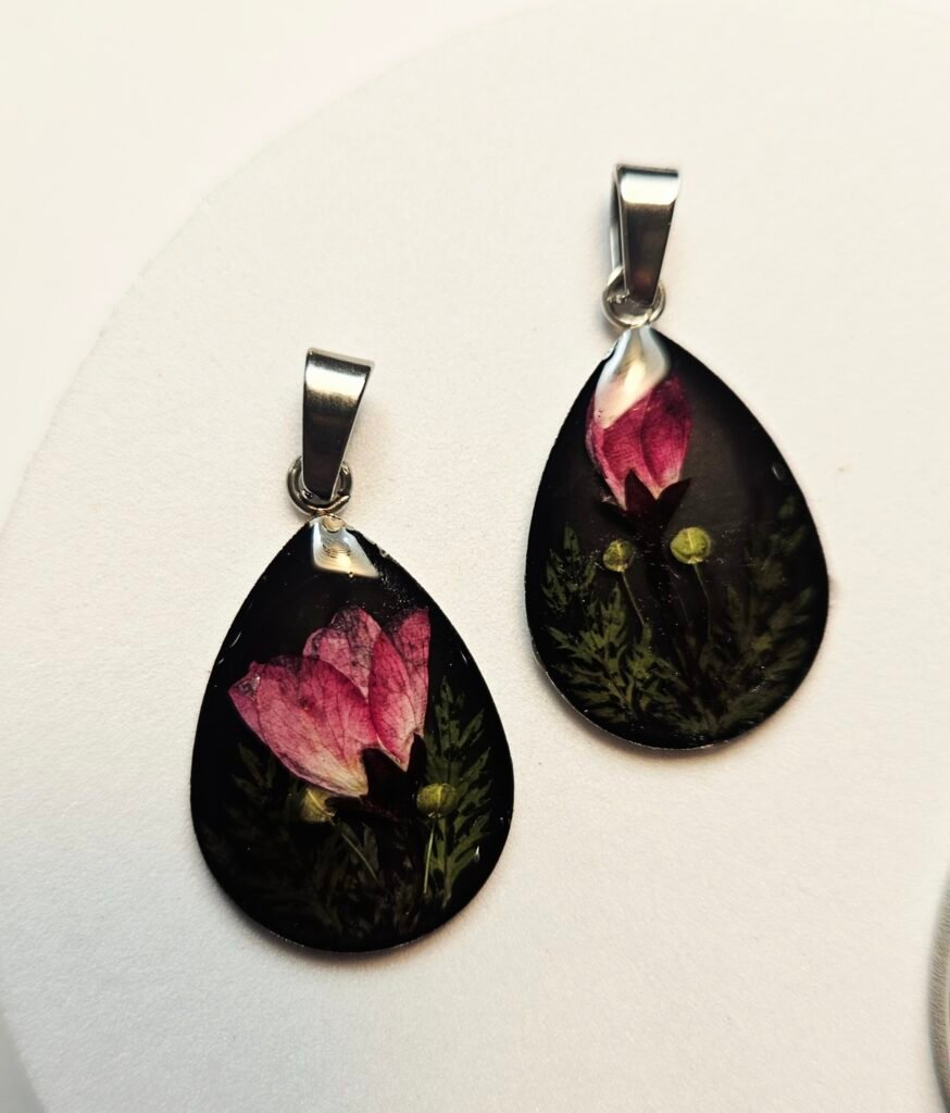 Tropfenförmige UV-Resin Anhänger mit rosa Trockenblüten und Farn auf schwarzem Grund, aus dem Schmuck-Workshop in Wuppertal
