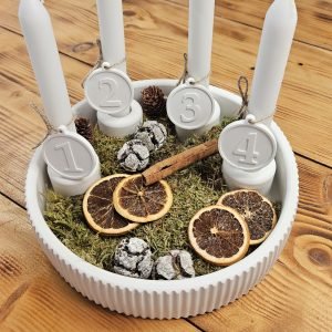 Adventskranz aus Gießkeramik: gerillte weiße Schale mit vier Kerzen, Zahlenanhängern 1–4, Moos, Orangenscheiben und Zapfen