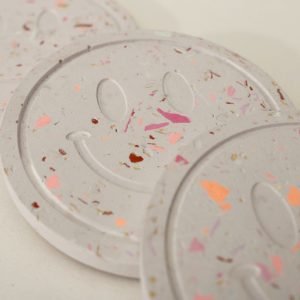 Drei Untersetzer aus Gießkeramik mit Smiley-Relief und Terrazzo-Muster in Rosa, Koralle und Gold, aus dem Workshop in Wuppertal
